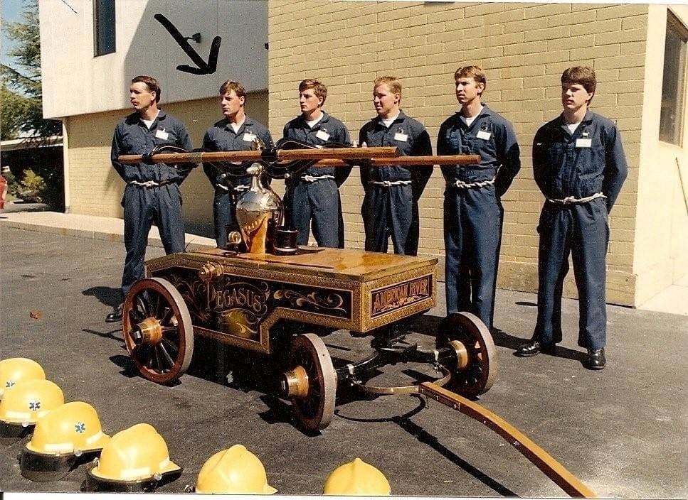 Recruit class standing behind an antique hand-pump fire cart