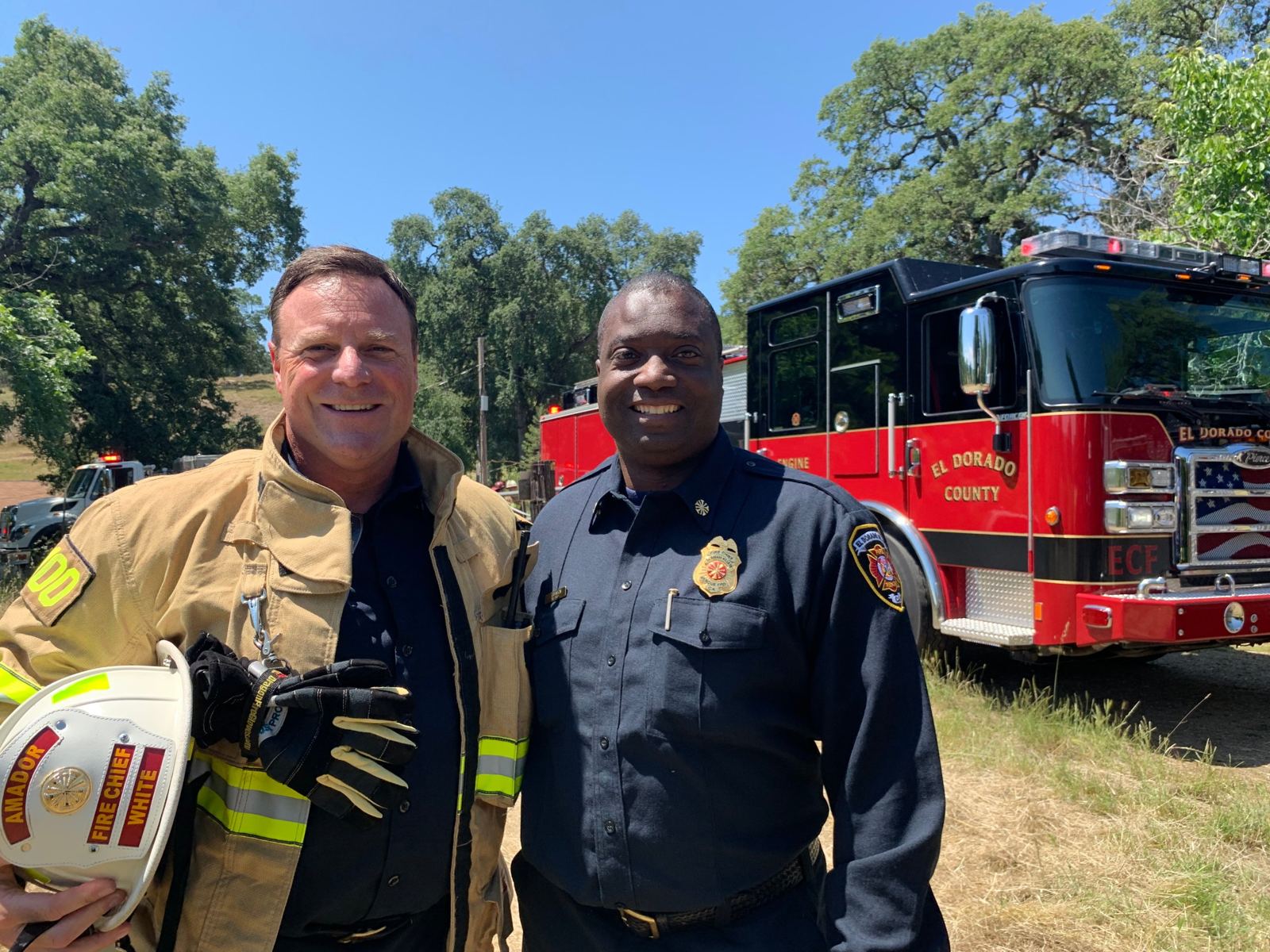 Chief White holding his Amador Fire Chief helmet beside an engine